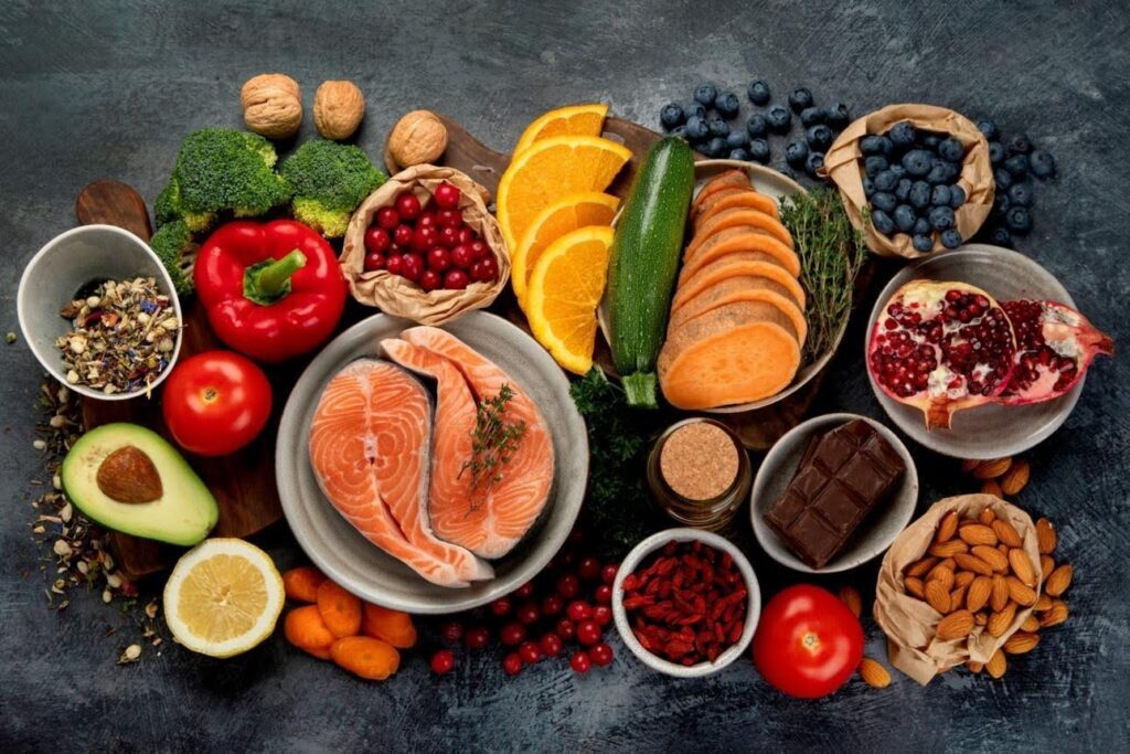 A variety of healthy whole foods including salmon, broccoli, red capsicum, berries, nuts, and dark chocolate